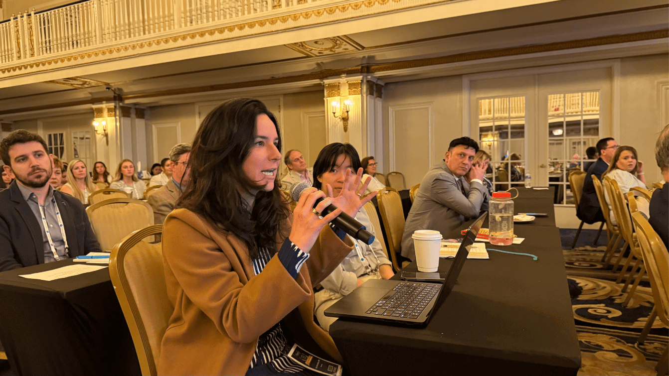 A woman speaking into a microphone at a conference table.